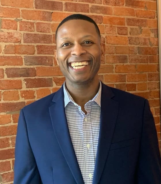 A man in a suit standing next to a brick wall.