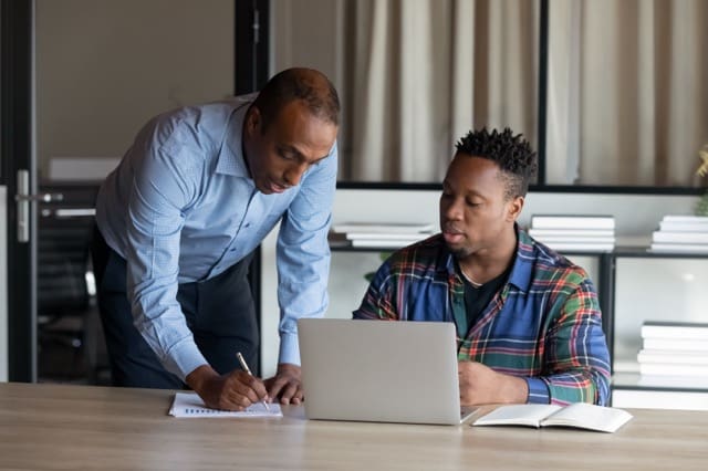 Two men are working on a laptop together.